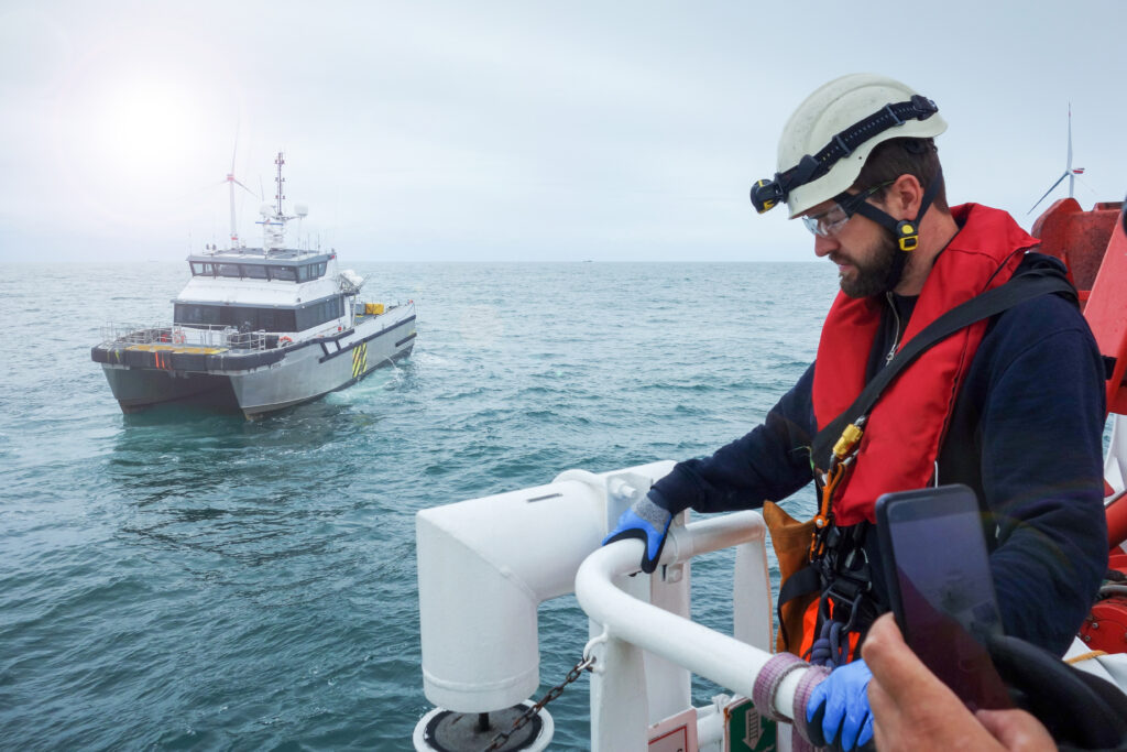 Offshore manual high worker waiting for transfer vessel with wind-turbines behind him.